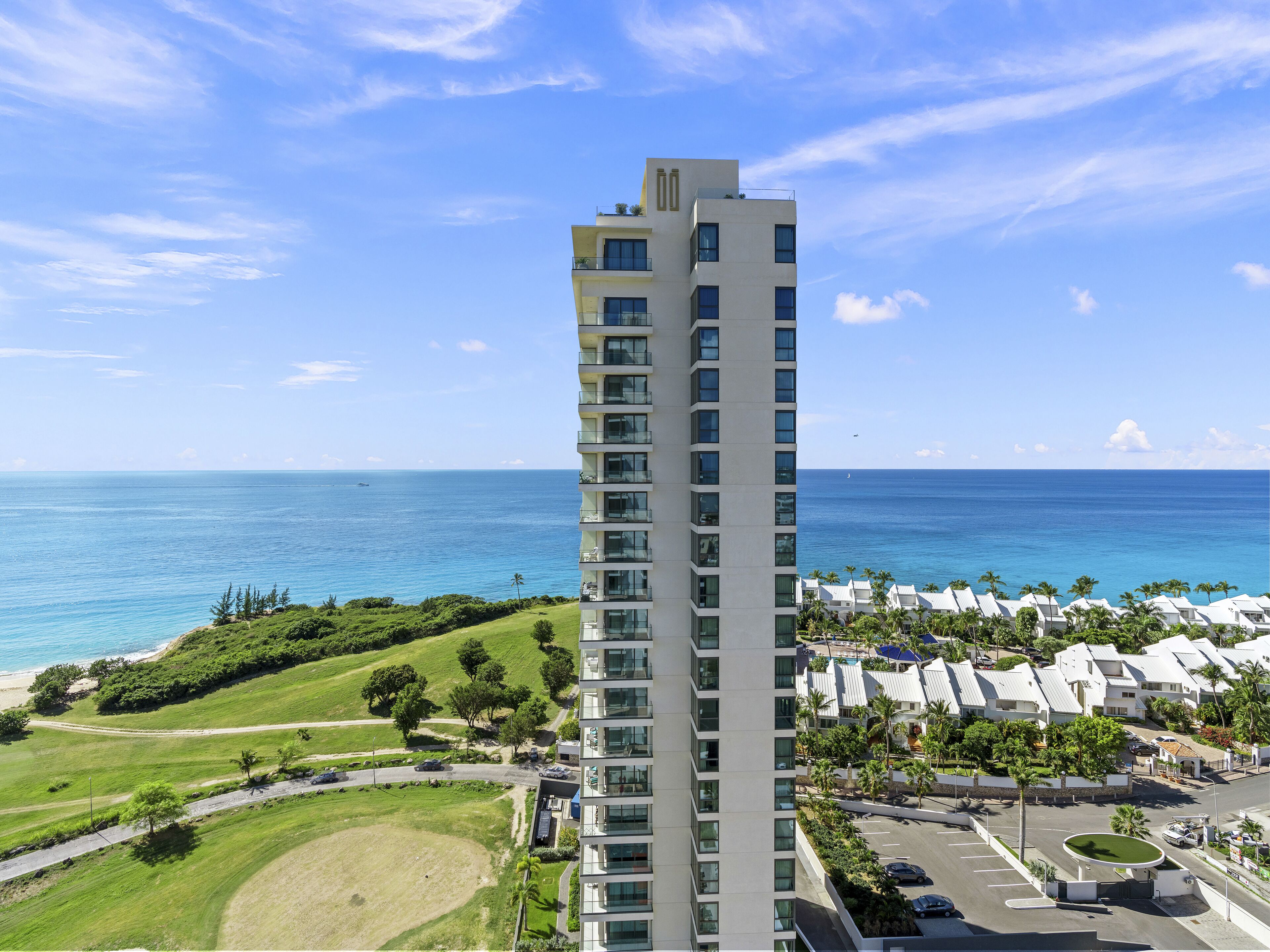 A high-rise hotel with a view of the ocean, featuring multiple balconies and a parking area.