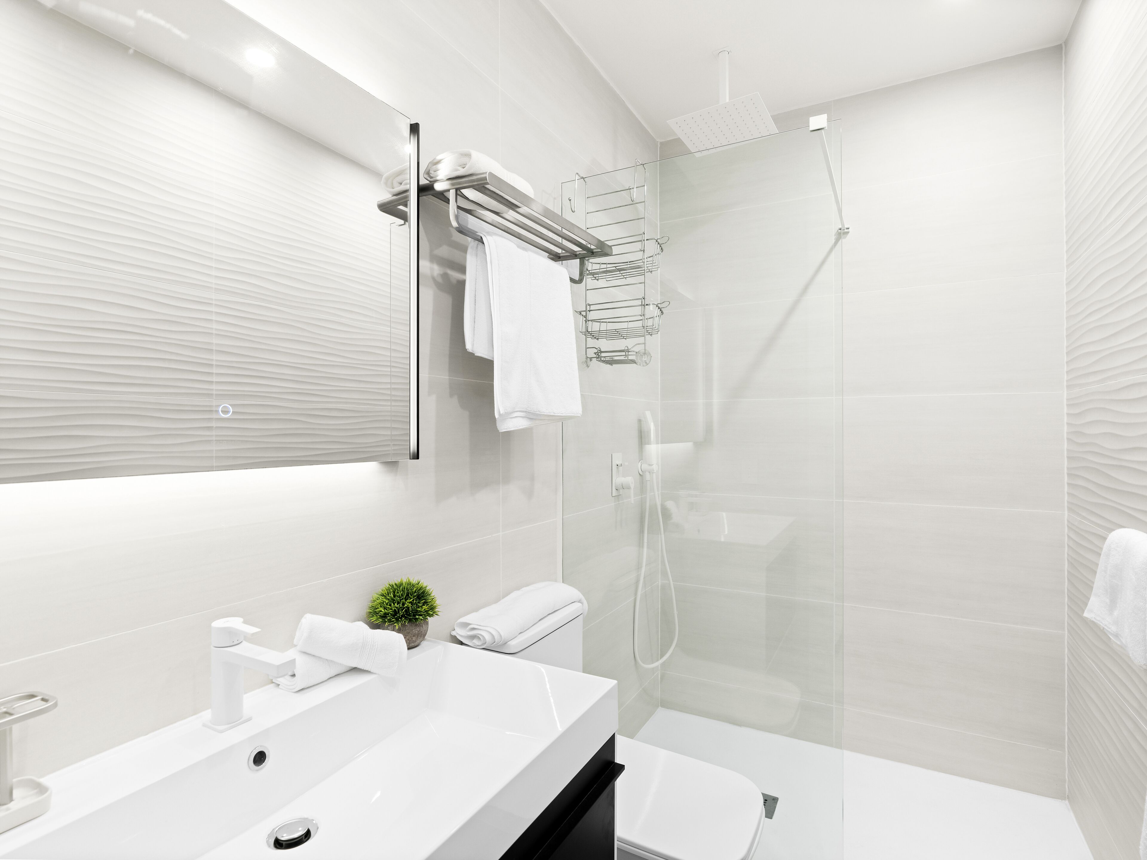 Un bagno moderno con uno specchio grande, una cabina doccia in vetro e un lavandino bianco con una pianta.