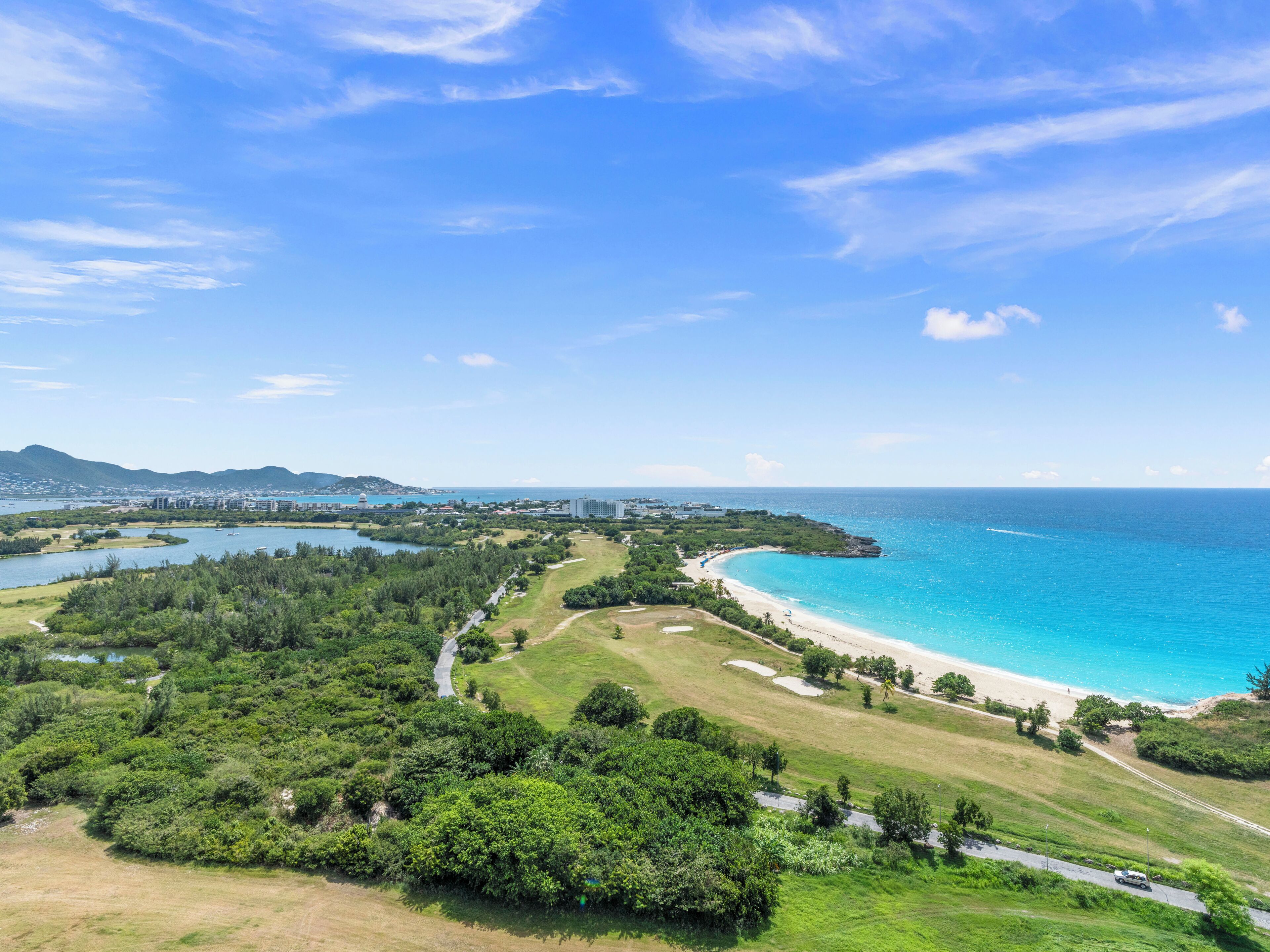 A coastal landscape with a beach, a golf course, and a city in the background.