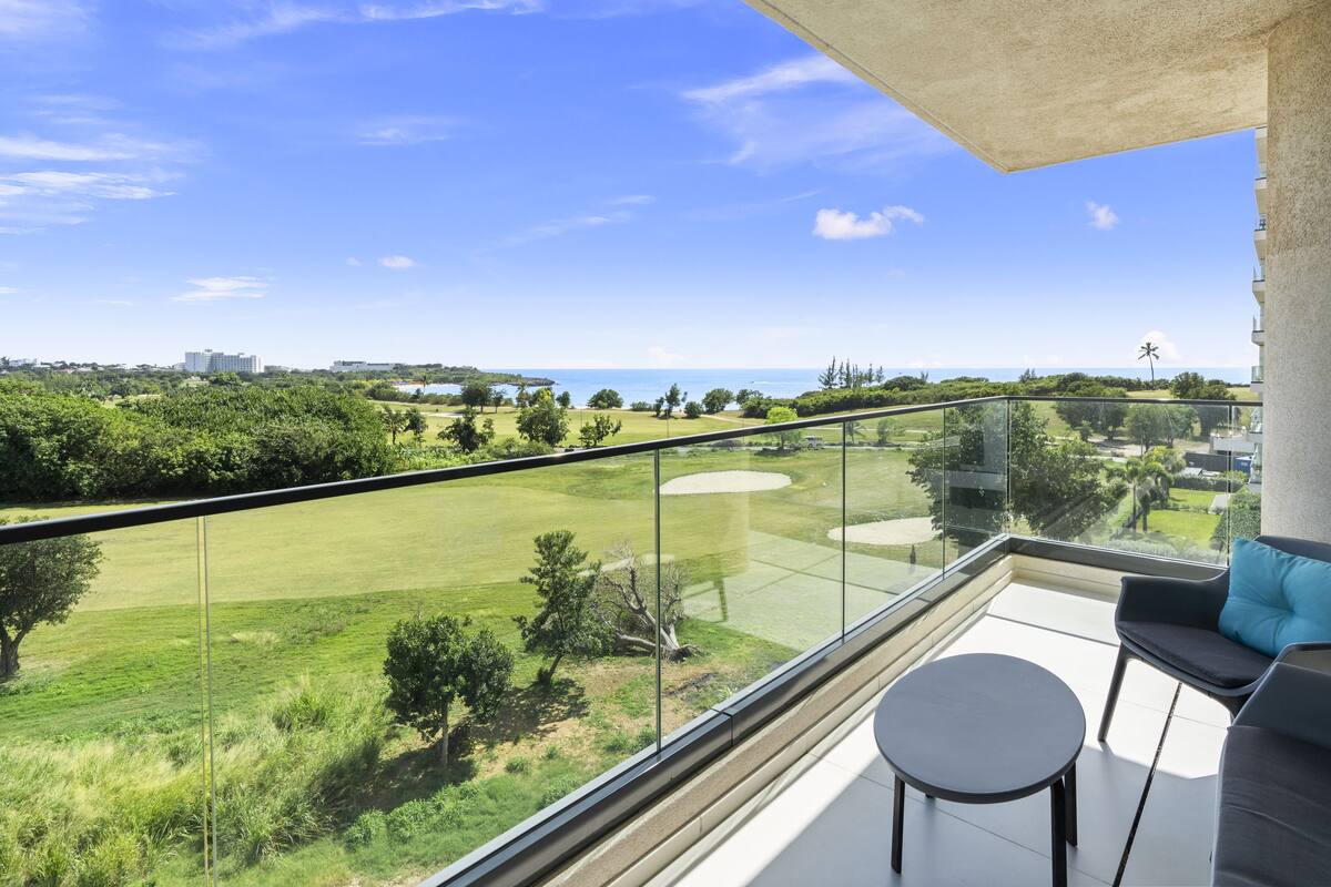Un balcon doté d’une balustrade en verre, offrant une vue sur un terrain de golf et l’océan.