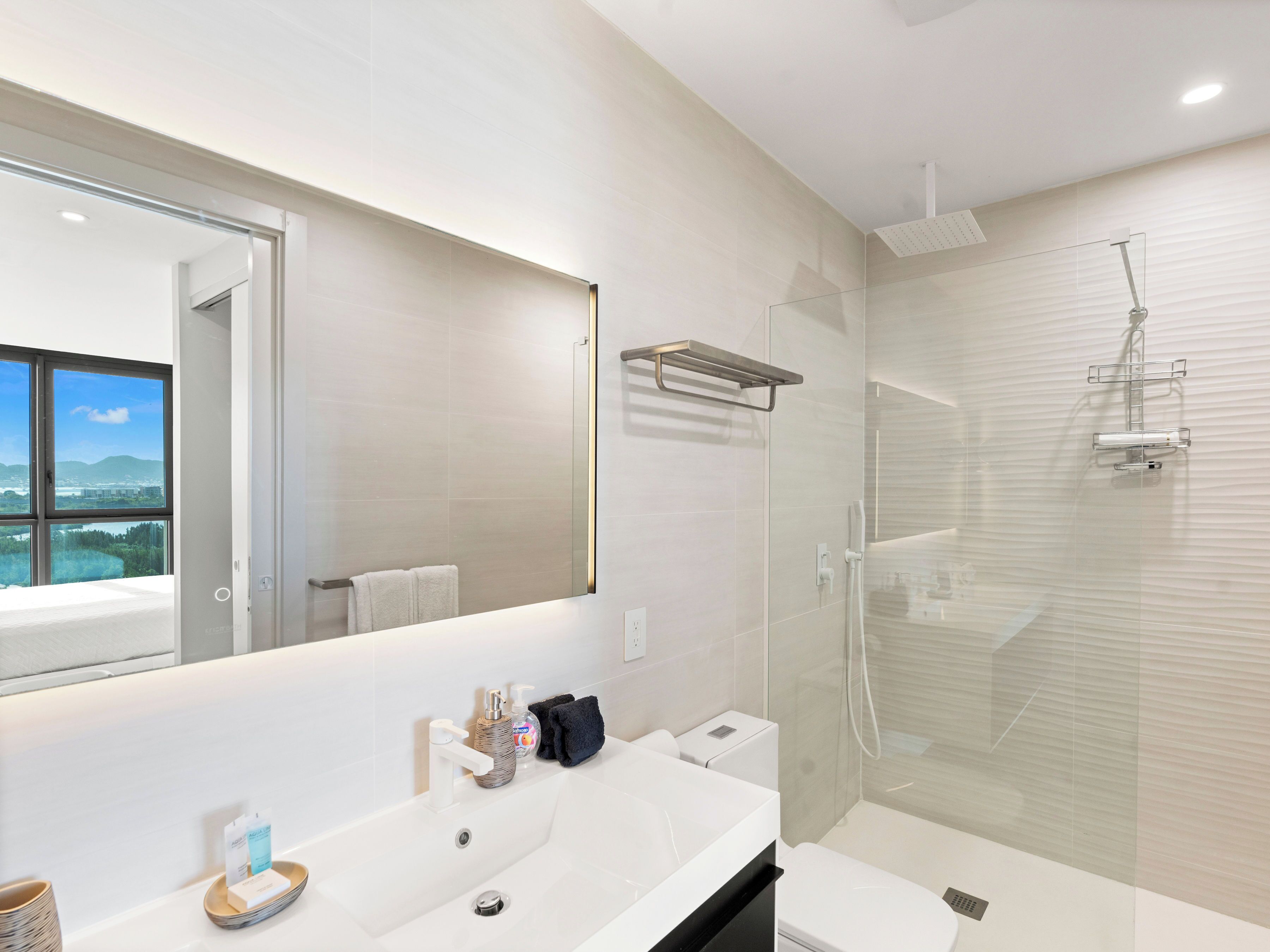Een moderne badkamer met een grote spiegel, een witte wastafel, een toilet en een douchecel met glazen wanden.