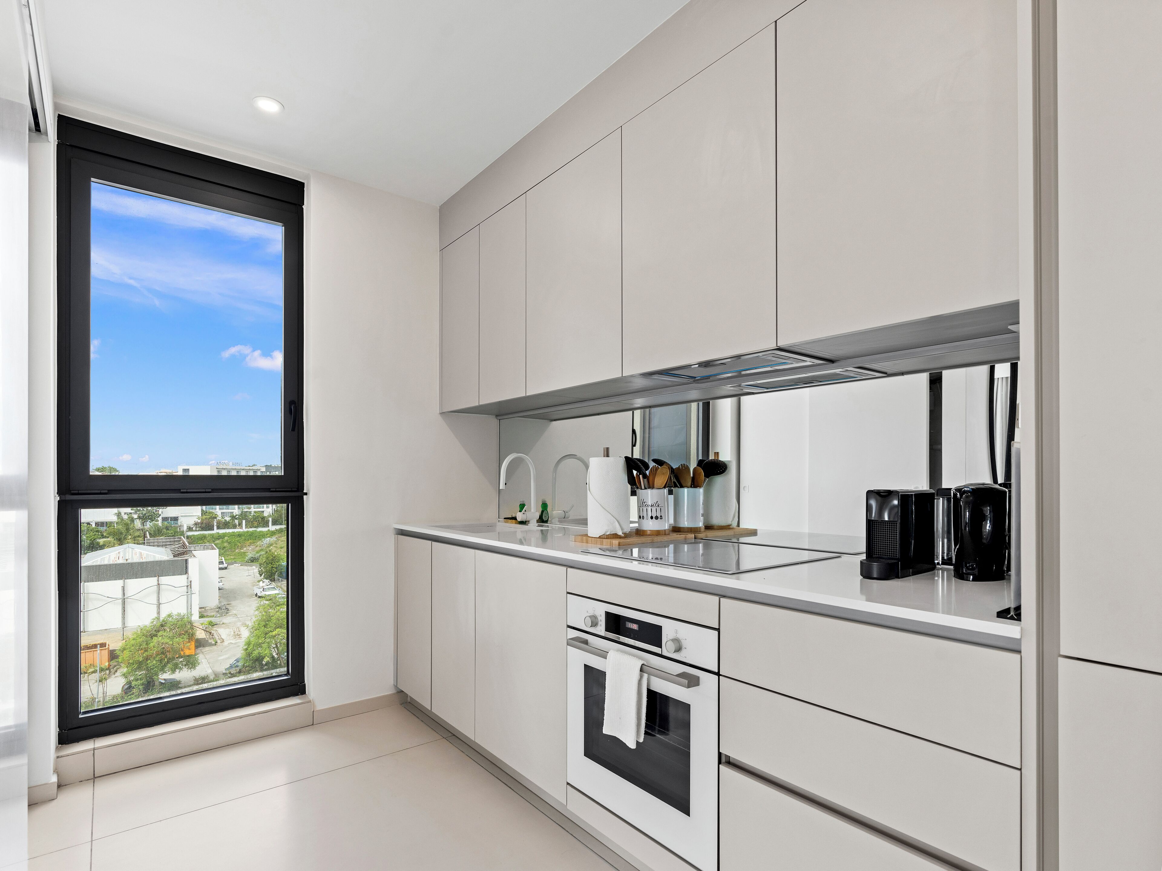 A modern kitchen with white cabinetry, a large window, and a view of the city.