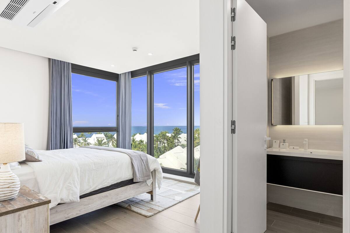 Une chambre d’hôtel moderne avec un grand lit, une salle de bain dotée d’un plan de toilette noir et une vue sur l’océan.