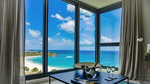 A room with a large window overlooking a beach and ocean, a table with a bottle of champagne, and a book. - Fourteen at Mullet Bay (Lowlands)