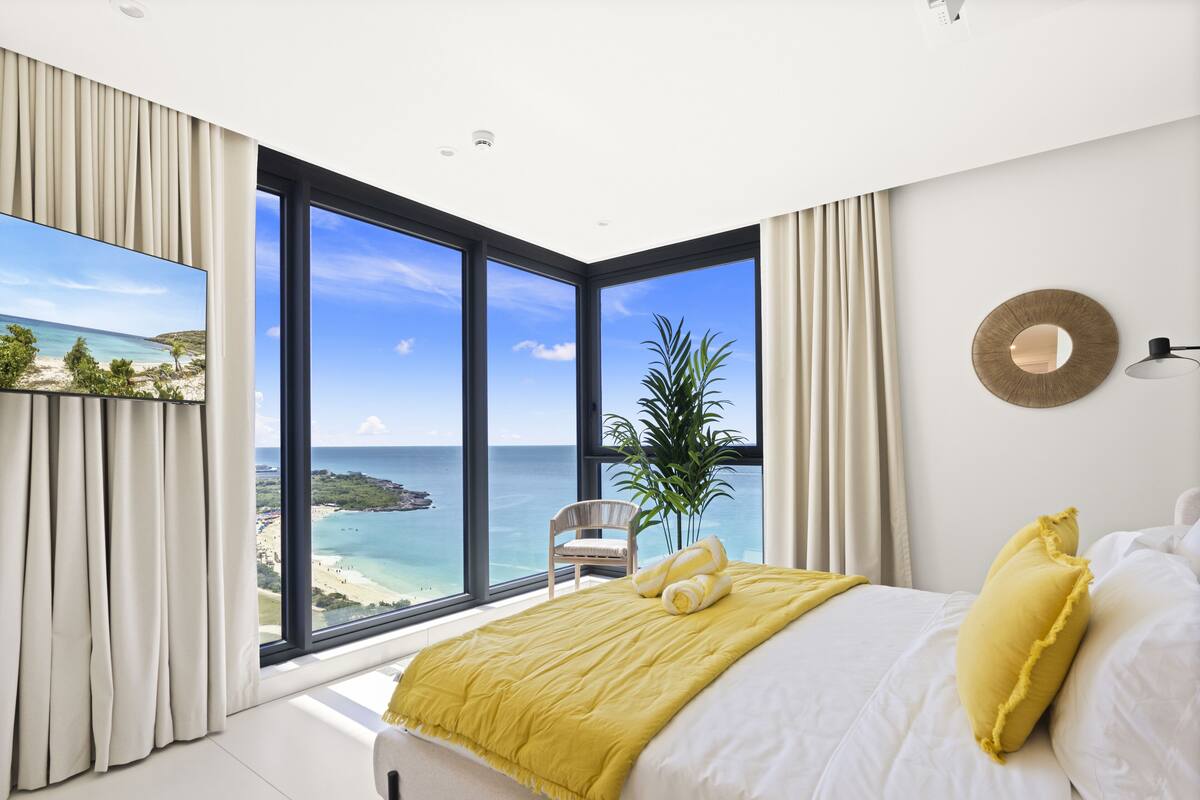 Une chambre avec une grande fenêtre donnant sur une plage et l’océan.