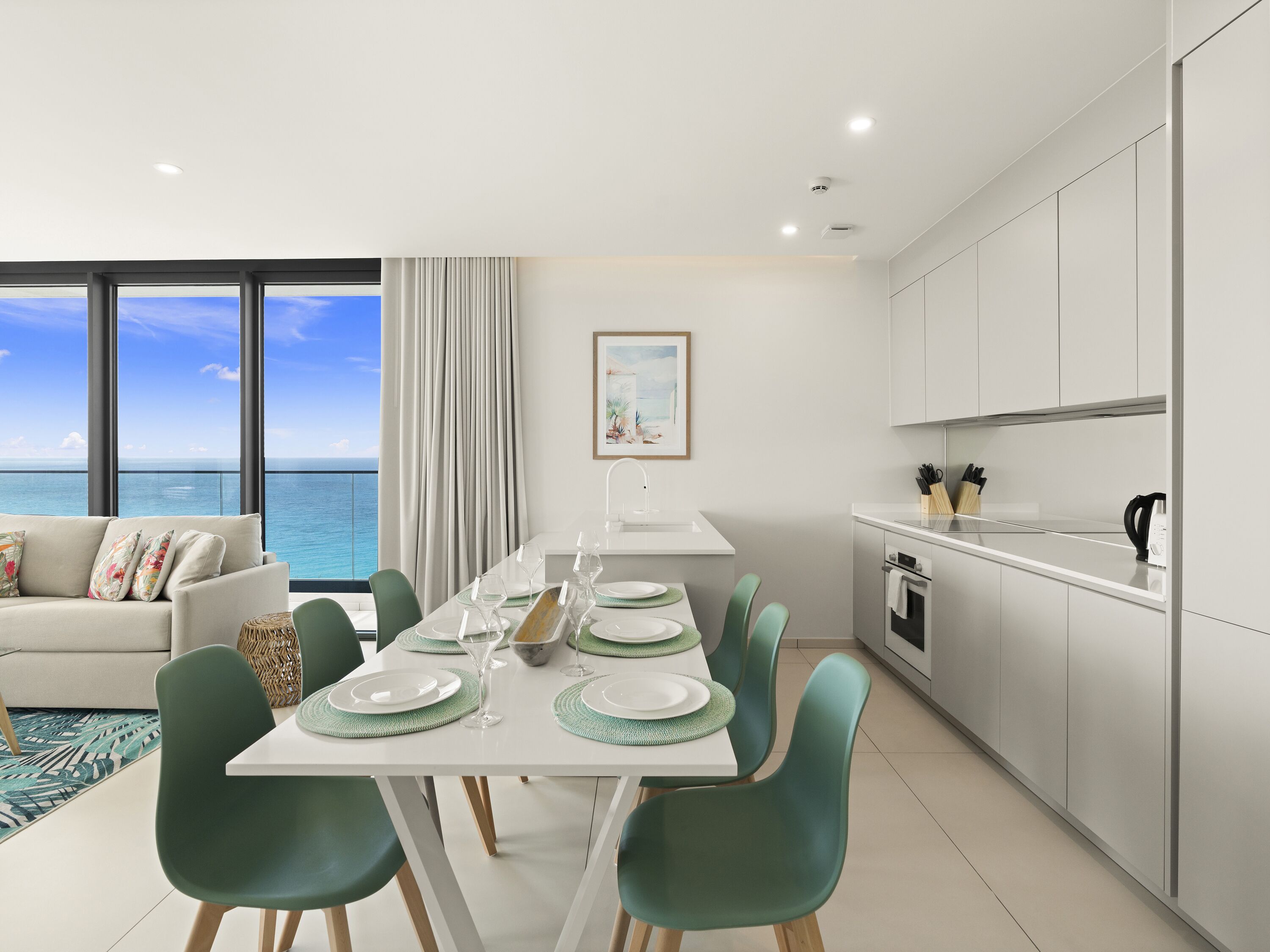 A modern dining area with a view of the ocean, a white kitchen with stainless steel appliances, and a cozy seating area with a view.
