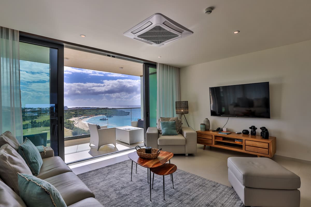 Un salon moderne doté d’un grand téléviseur, de sièges confortables et offrant une vue sur la plage.