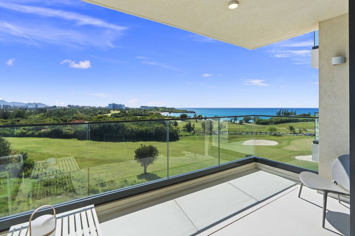 Un balcon offrant une vue dégagée sur un terrain de golf, l’océan et les bâtiments situés au loin.