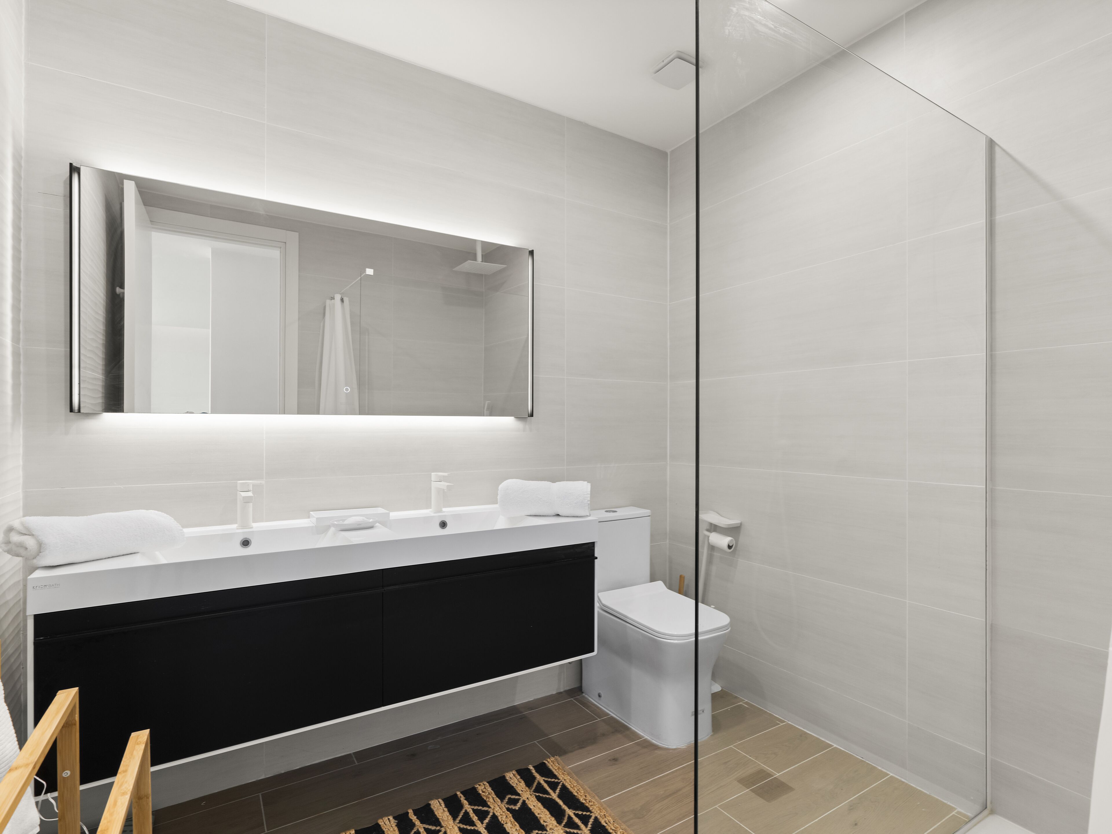 A modern bathroom with a large mirror, a black vanity, a toilet, and a shower area.