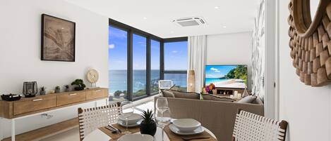 A modern dining area with a view of the ocean, a wooden dining table set with plates and cutlery, and a white console table with decorative items.