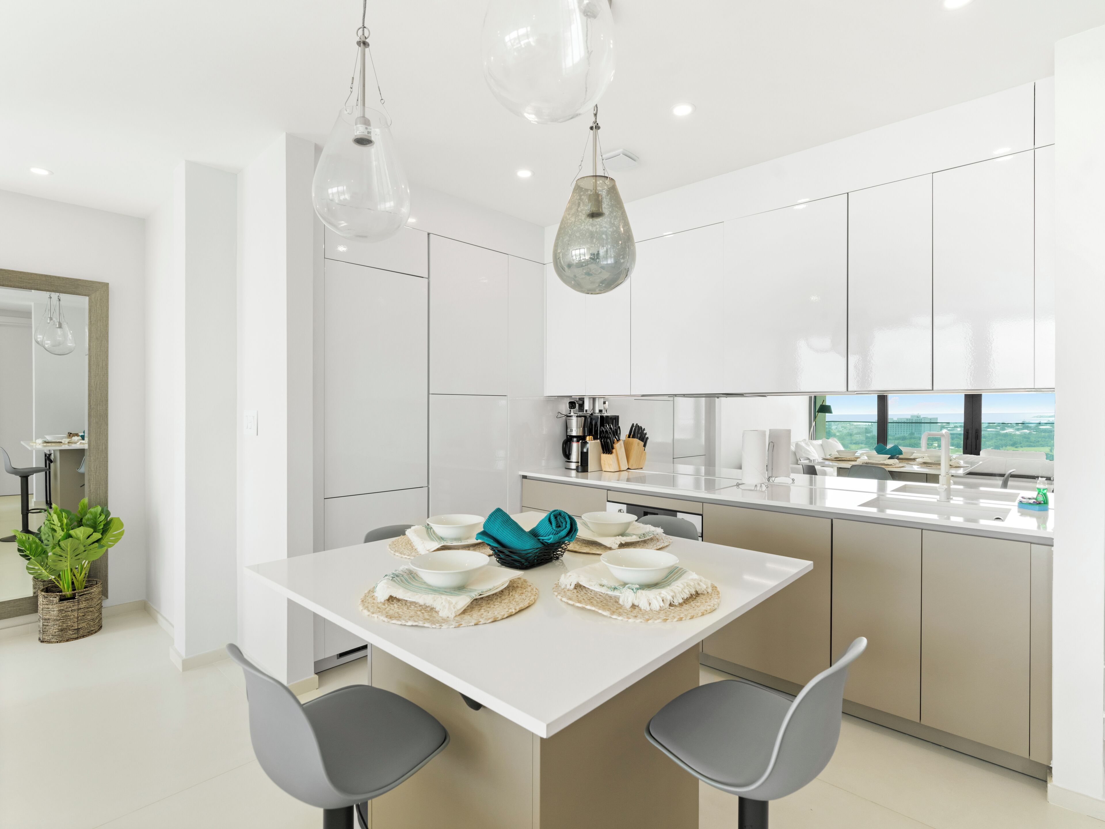 A modern kitchen with white cabinets, a dining table with two chairs, and hanging pendant lights.