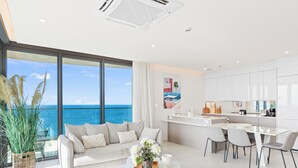A modern living room with a large window overlooking the ocean, a dining area, and a kitchen with white cabinetry. - Fourteen at Mullet Bay (Lowlands)