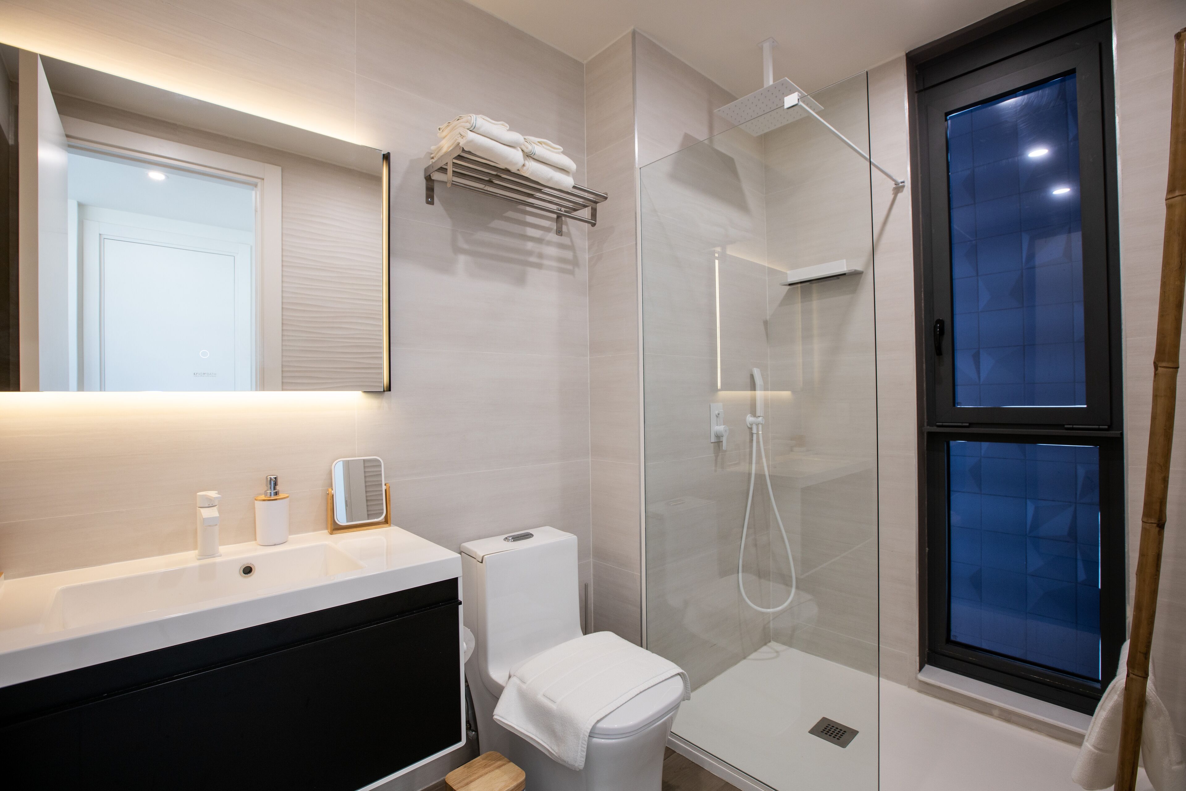Et moderne badeværelse med et brusebad i glas, toilet, håndvask med spejl og et håndklædestativ.