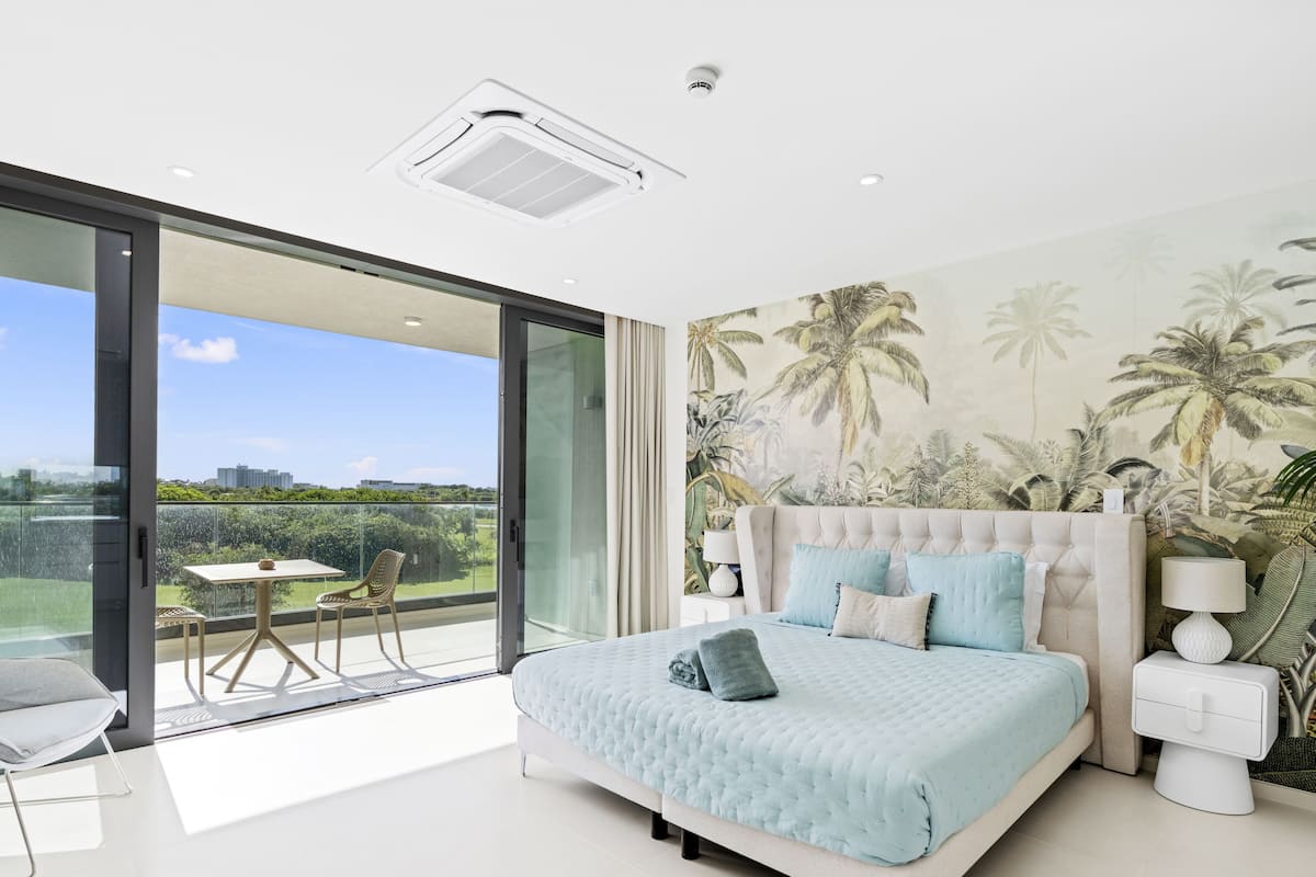 Une chambre avec un grand lit, un balcon avec une table et des chaises, et une fresque murale aux motifs tropicaux.