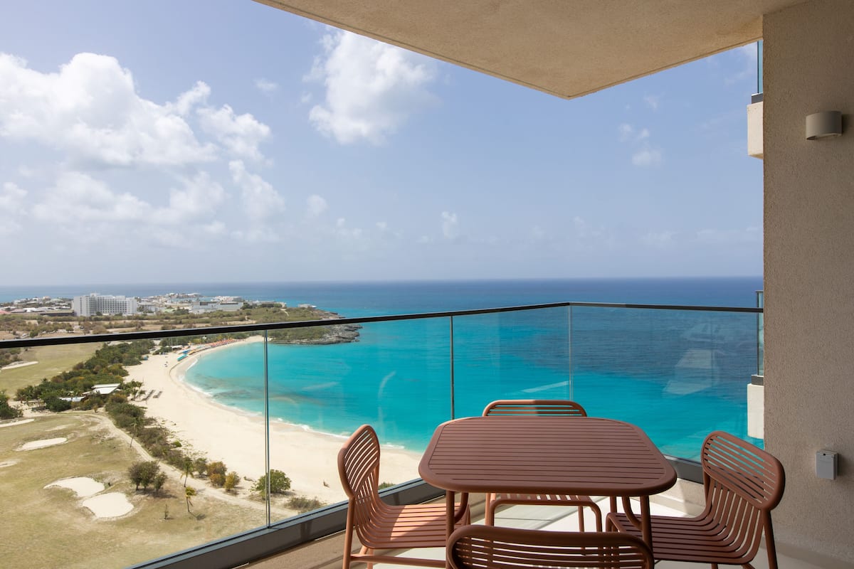 Un balcon avec une table et des chaises donnant sur une plage et l’océan.
