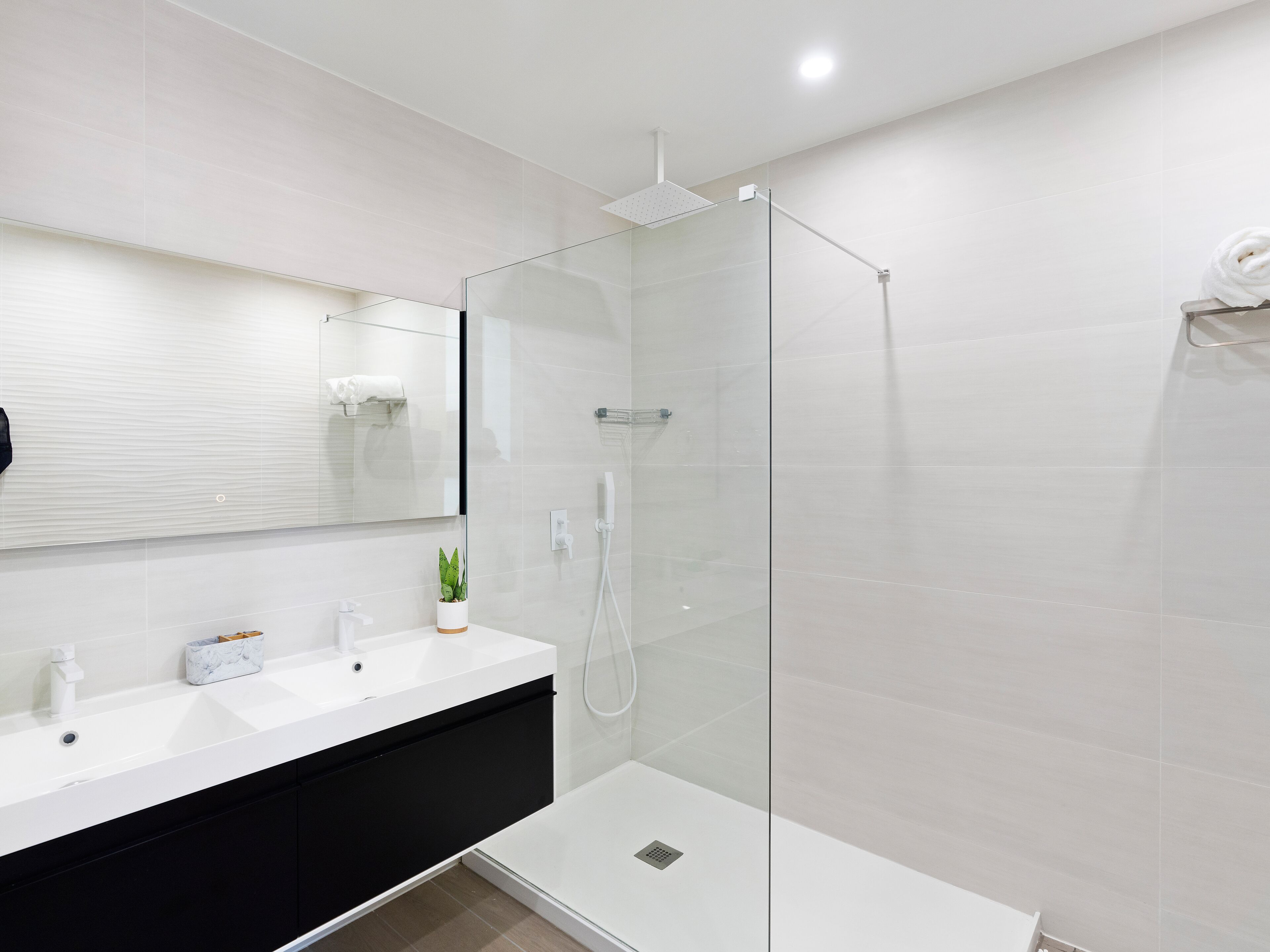 Un baño moderno con cabina de ducha de vidrio, un lavabo blanco y un mueble de tocador negro.