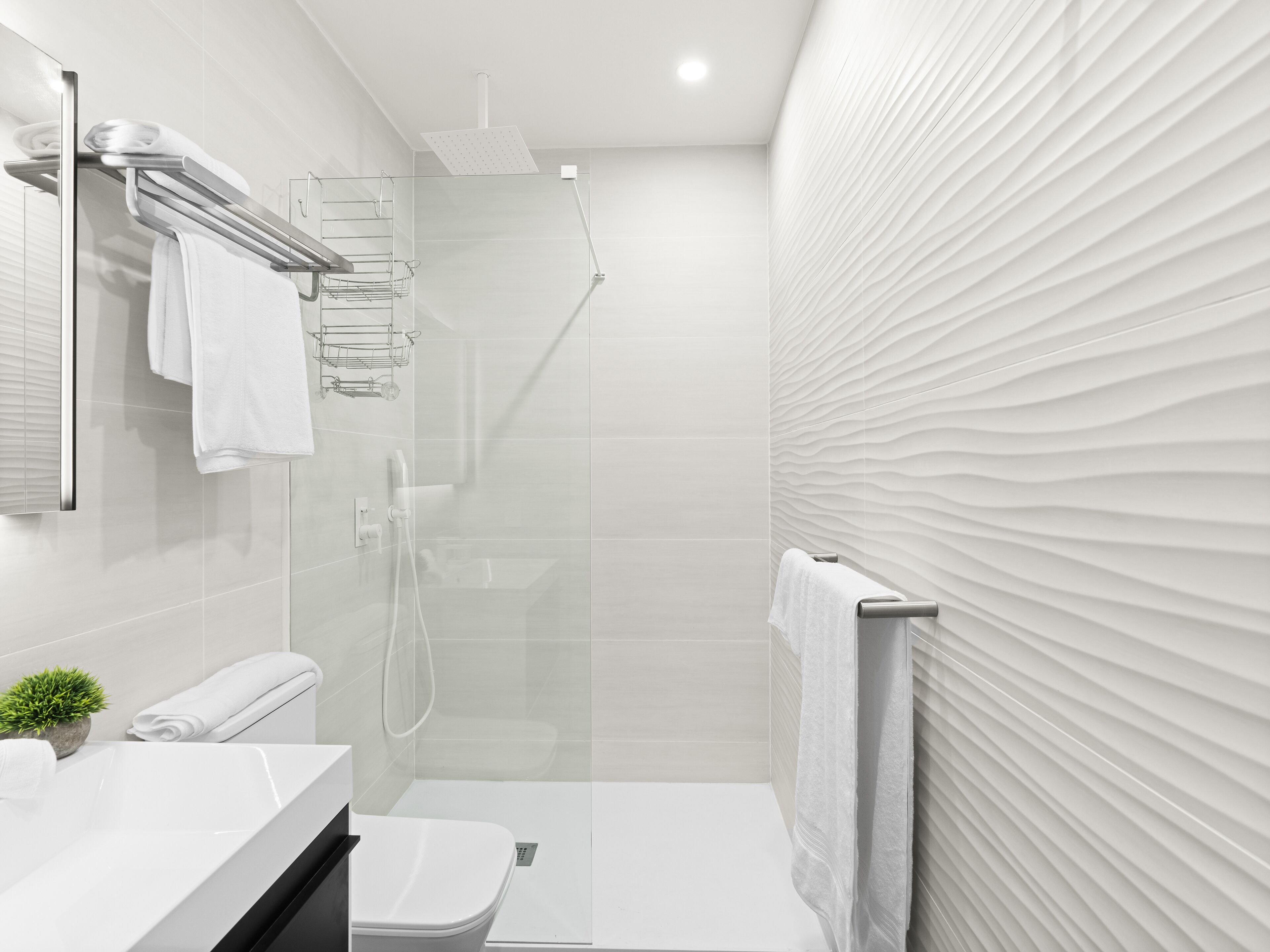A modern bathroom with a glass-enclosed shower, a toilet, and a sink with a mirror.