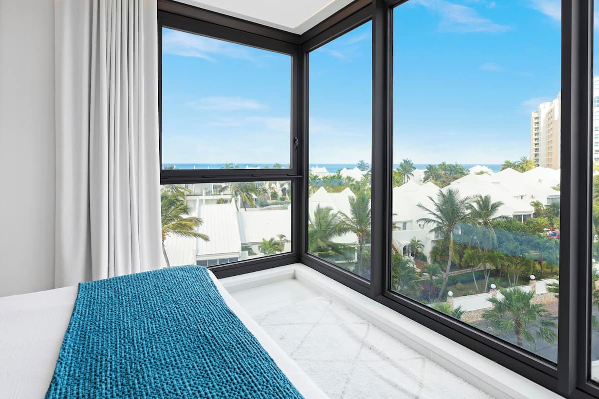 Une chambre d’hôtel dotée d’une grande fenêtre donnant sur la plage et les palmiers.