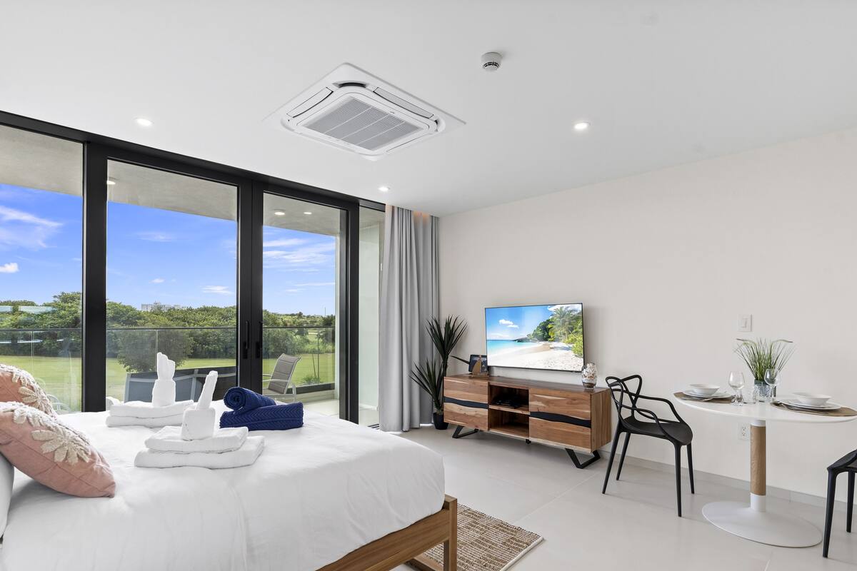 Une chambre moderne dotée d’un grand lit, d’un bureau avec un téléviseur à écran plat et d’un balcon offrant une vue sur la plage.