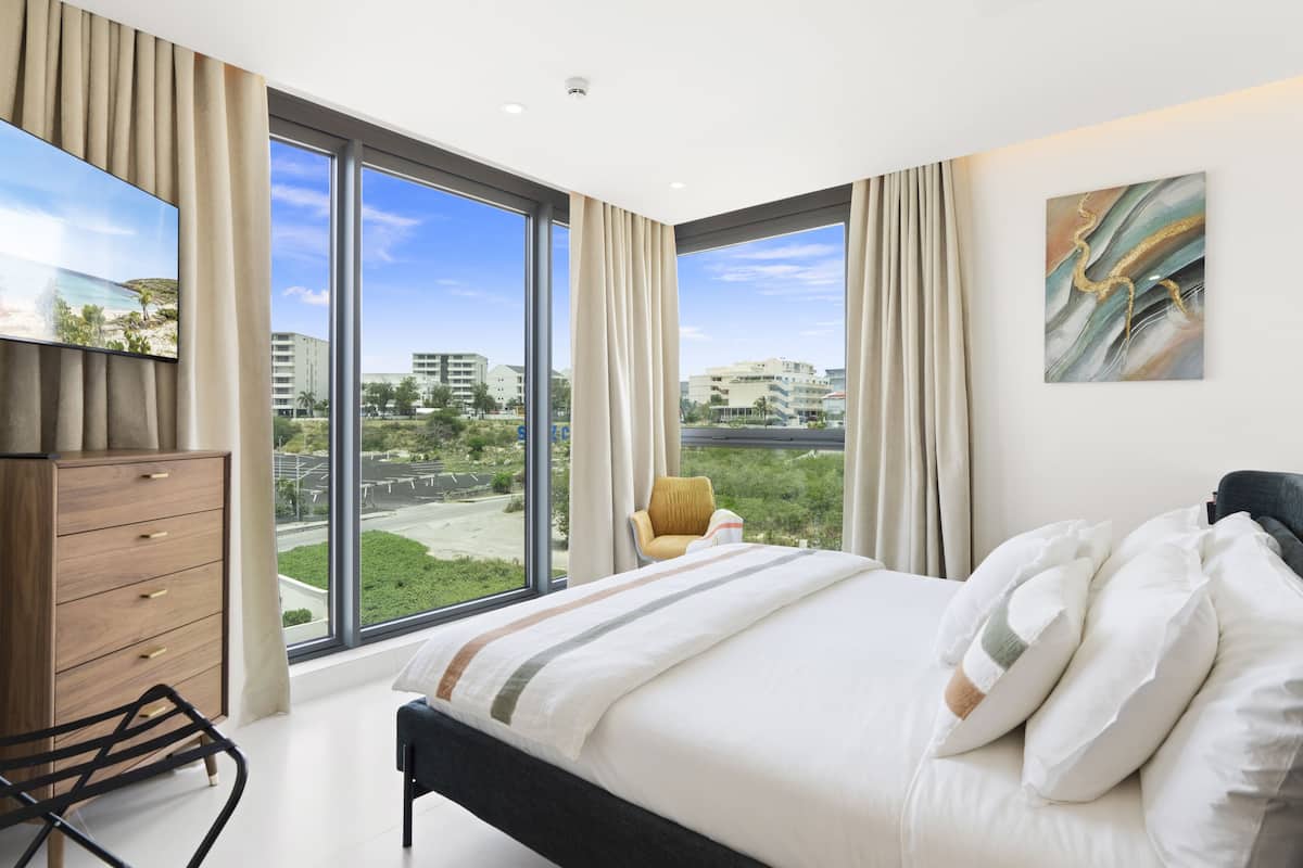 Une chambre d’hôtel moderne avec un grand lit, une commode en bois, une chaise et un téléviseur.