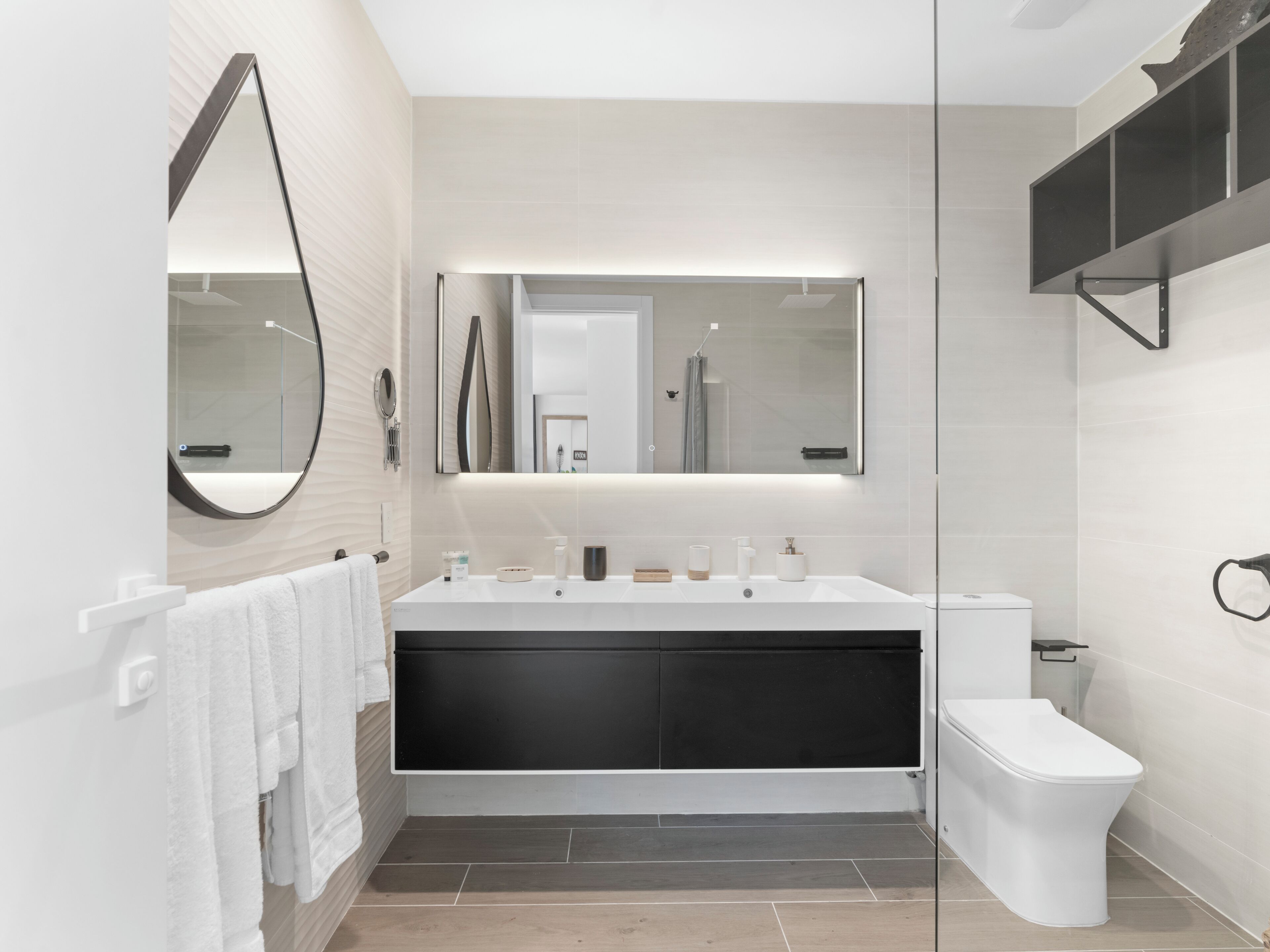 A modern bathroom with a large mirror, a vanity with a black sink, and a toilet.