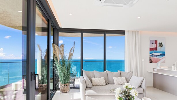 A modern living room with a large glass door leading to a balcony overlooking the sea. - Fourteen at Mullet Bay (Lowlands)