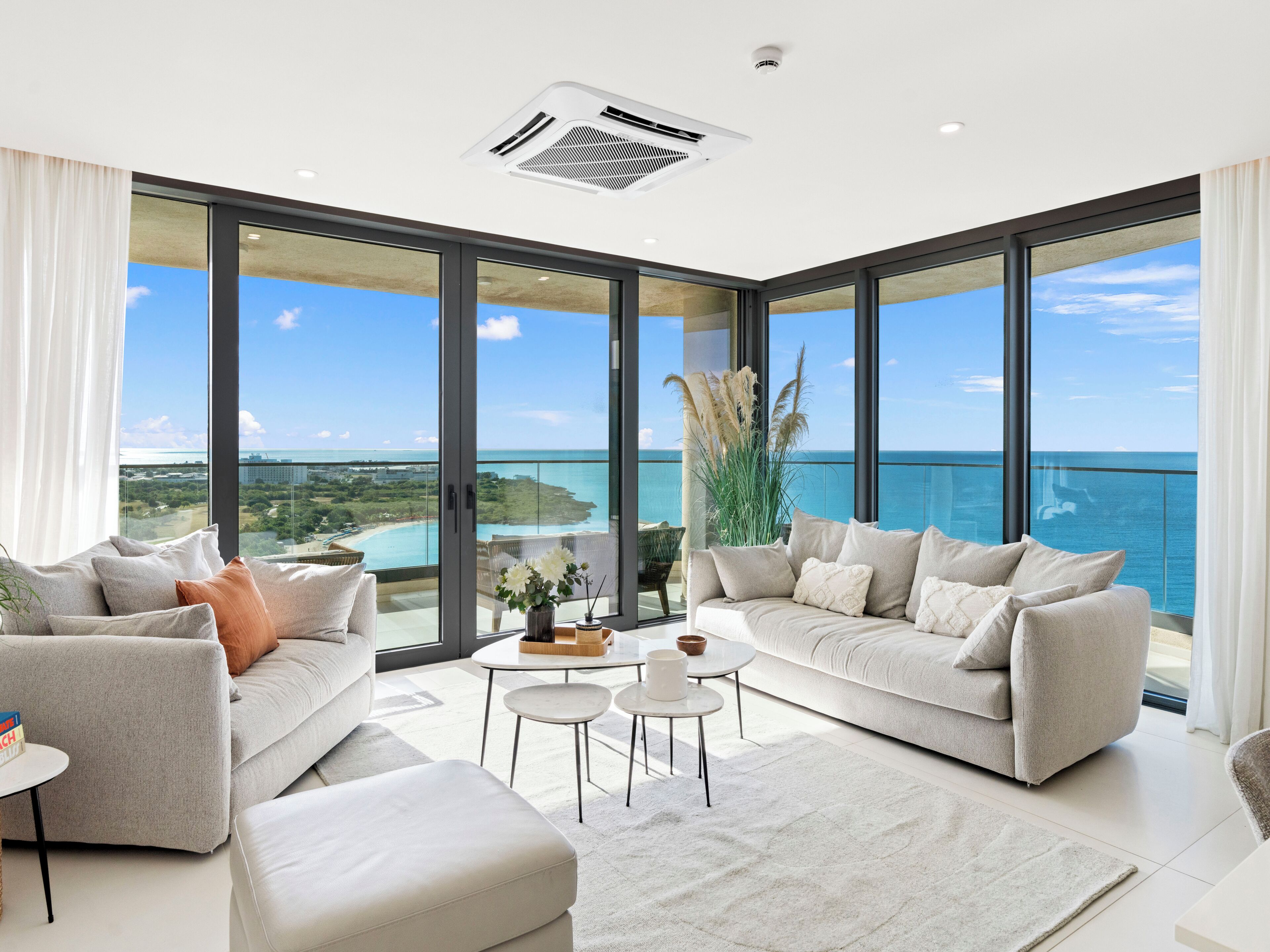 A spacious living room with a large window offering a view of the ocean and a distant cityscape.