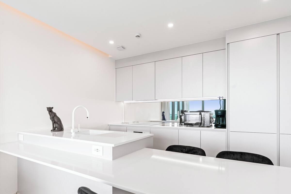 Une cuisine moderne avec des meubles blancs, un grand îlot central doté d’un évier et d’une machine à café.