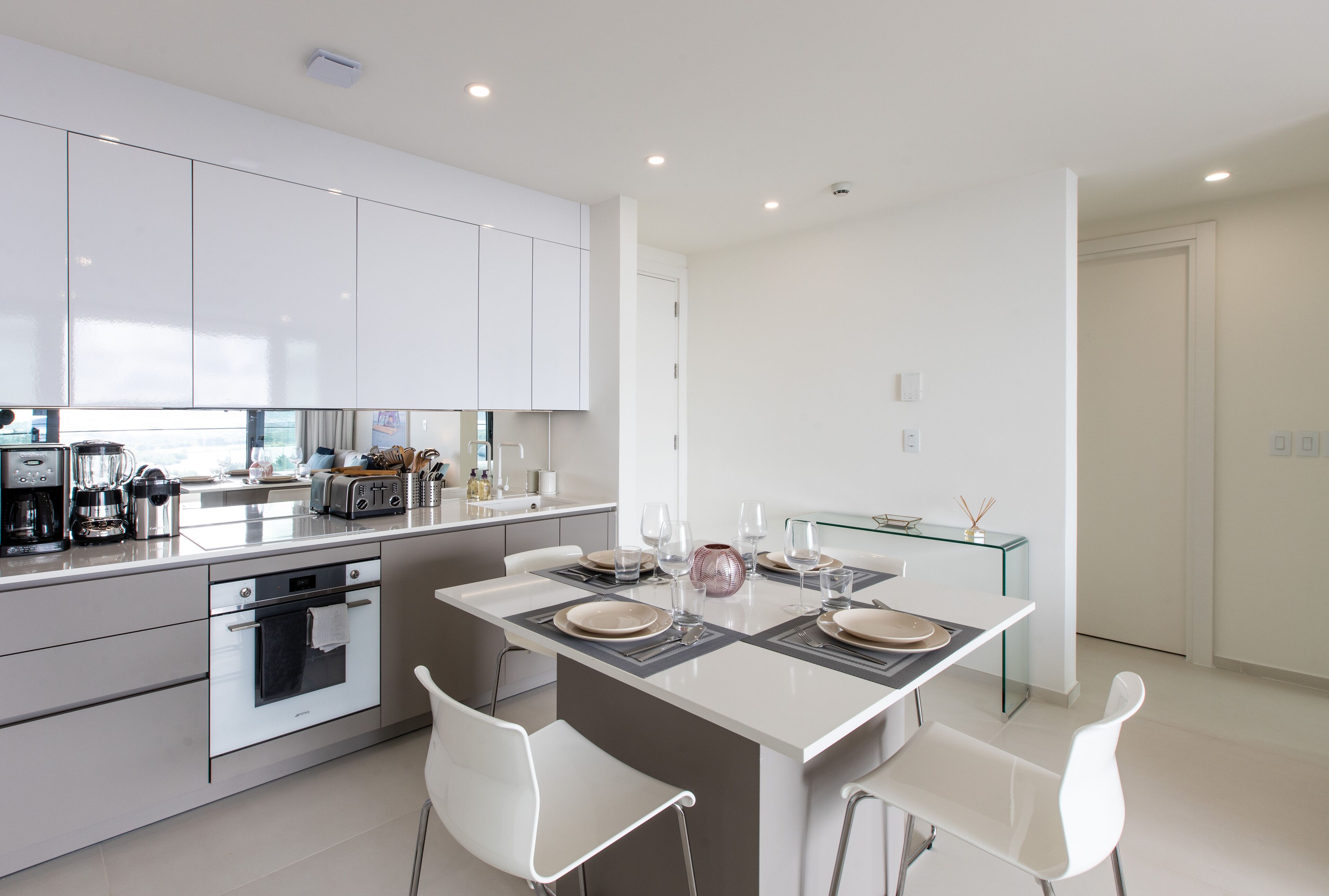 A modern kitchen with white cabinets, a central island with seating, and a glass dining table.