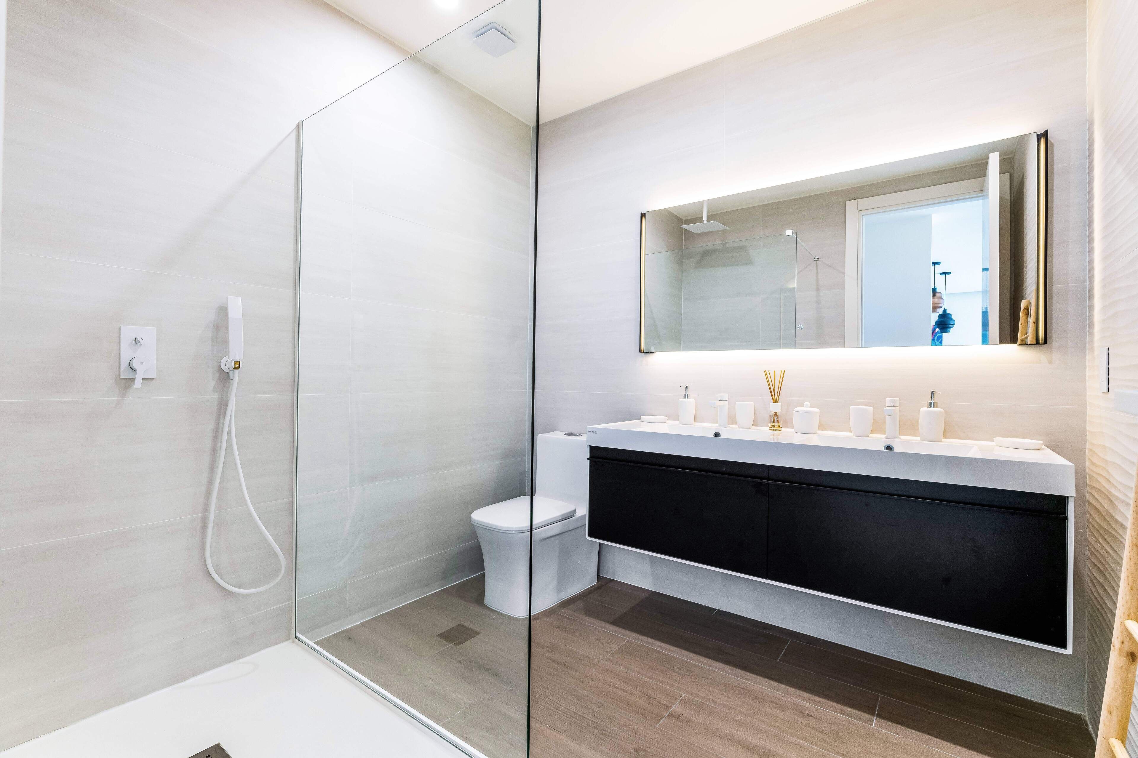A modern bathroom with a glass shower enclosure, a white toilet, a black vanity with a mirror, and a white sink.