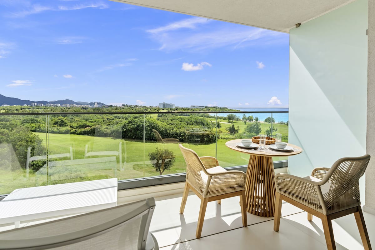 Un balcon avec une table et des chaises, donnant sur un paysage verdoyant et luxuriant et sur une étendue d’eau.