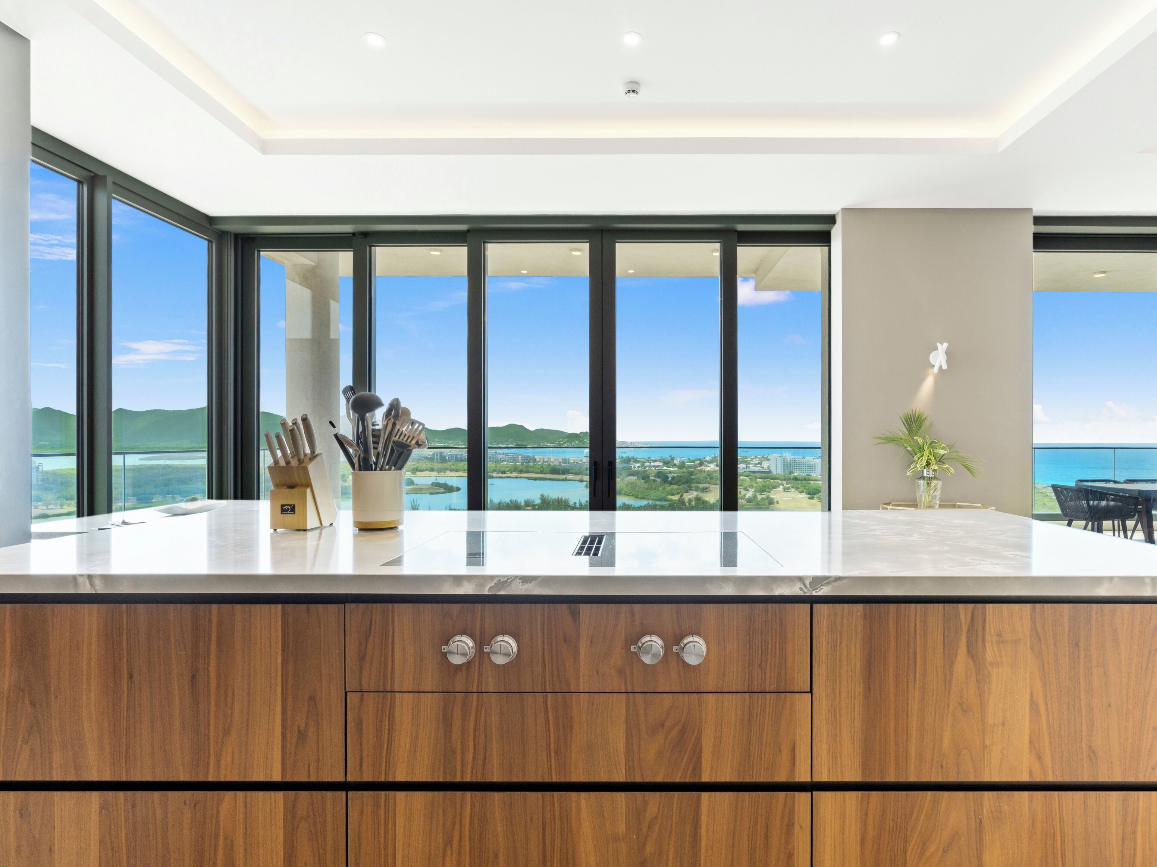 Een moderne keuken met een groot eiland, uitzicht op water en een eethoek met een tafel en stoelen.