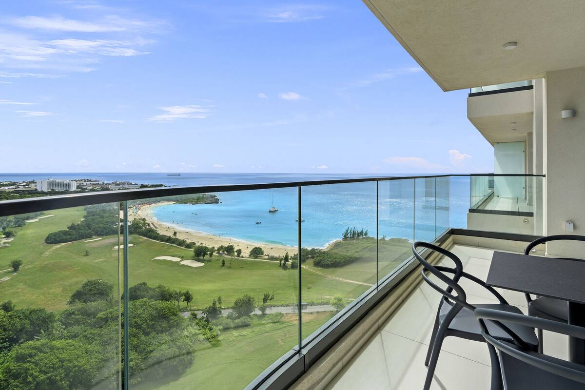 Un balcon offrant une vue dégagée sur une plage et l’océan, un terrain de golf et des bâtiments situés au loin.
