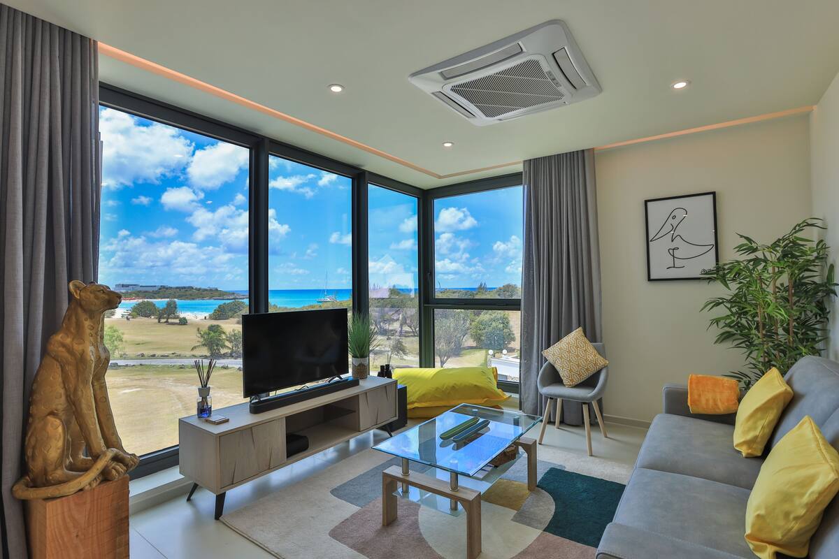 Un salon moderne doté d’une grande fenêtre donnant sur la plage et l’océan.