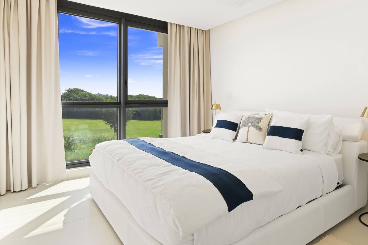 Une chambre moderne avec un grand lit, une vue sur un paysage verdoyant et un luminaire au plafond.