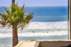 A beach view with palm trees, ocean waves, and people swimming.