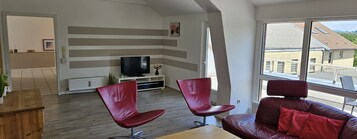 Una sala de estar moderna con un ventanal grande, un televisor y dos sillones rojos.