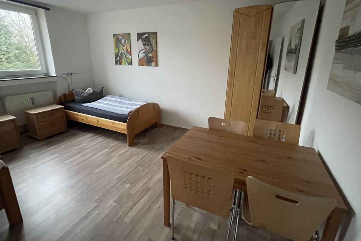 Ein Schlafzimmer mit einem hölzernen Bett, einem Schreibtisch, einem Stuhl, einem Kleiderschrank und zwei Wandbildern.