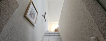 Una escalera estrecha con un cuadro en la pared y una fuente de luz en la parte superior.
