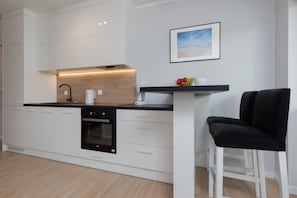 Una cucina moderna con mobili bianchi, un piano di lavoro nero, forno integrato, macchina da caffè e un quadro appeso al muro.