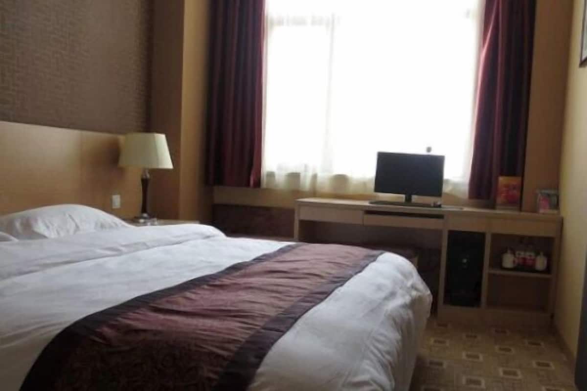Une chambre d’hôtel avec un lit, un bureau équipé d’un ordinateur et une fenêtre avec des rideaux.