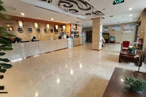 Zona de recepción de hotel con mostrador de mármol, luces empotradas en la pared y un piso limpio y pulido.