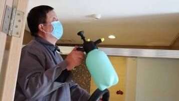 A person using a handheld device, possibly for cleaning or maintenance, in a room with a tiled wall and a light fixture on the ceiling.