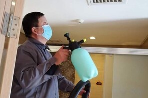 Une personne utilise un appareil portatif, peut-être pour nettoyer ou effectuer des travaux d’entretien, dans une pièce dont un mur est recouvert de carreaux et où un luminaire est fixé au plafond.