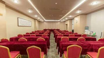 A conference room with rows of tables and chairs, a carpeted floor, and a framed picture on the wall.