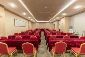 Une salle de conférence avec des rangées de tables et de chaises, un sol recouvert de moquette et un tableau encadré accroché au mur.