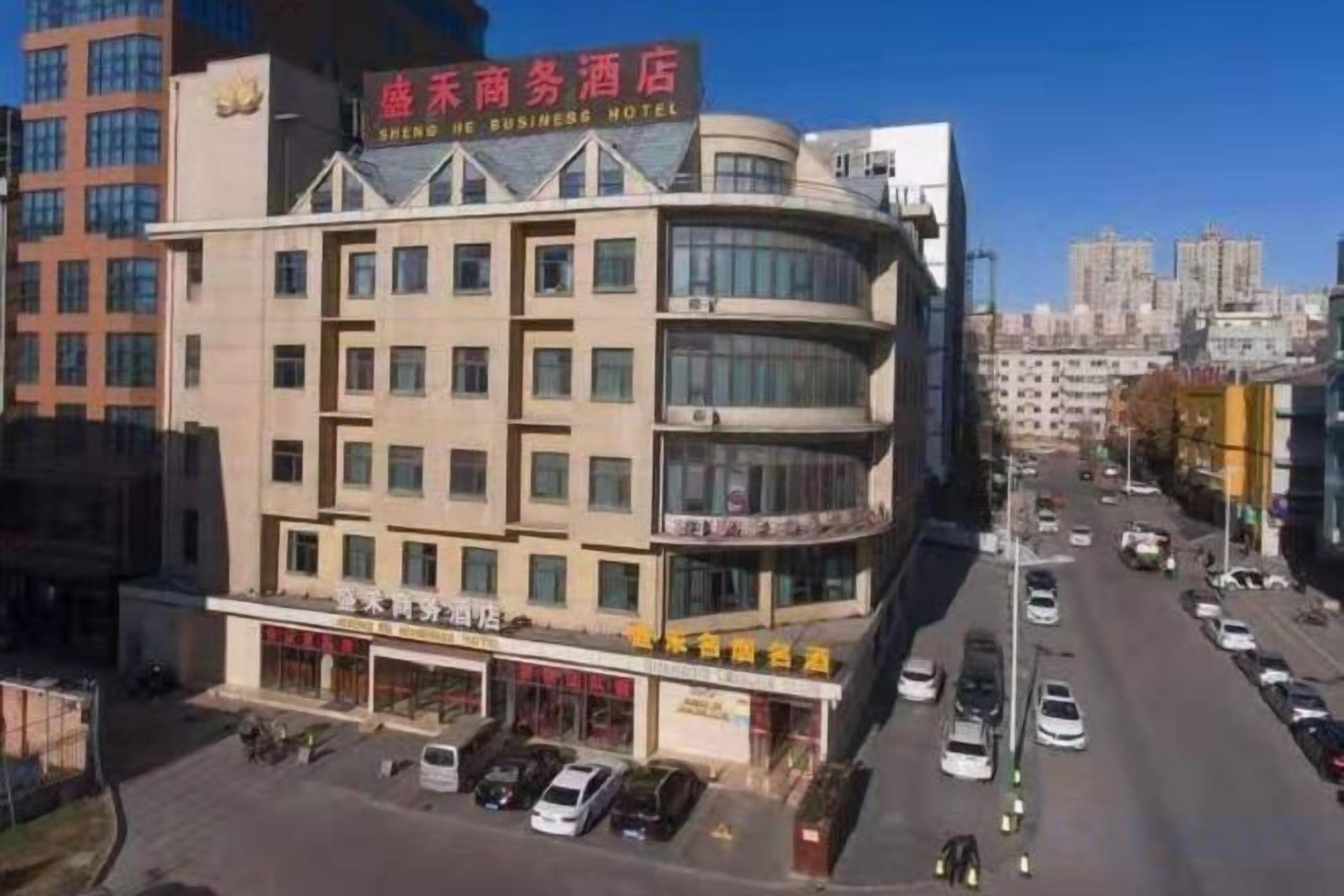 A multi-story hotel with a prominent signage indicating it is a business hotel. There are several ground-level shops and a parking area in front.