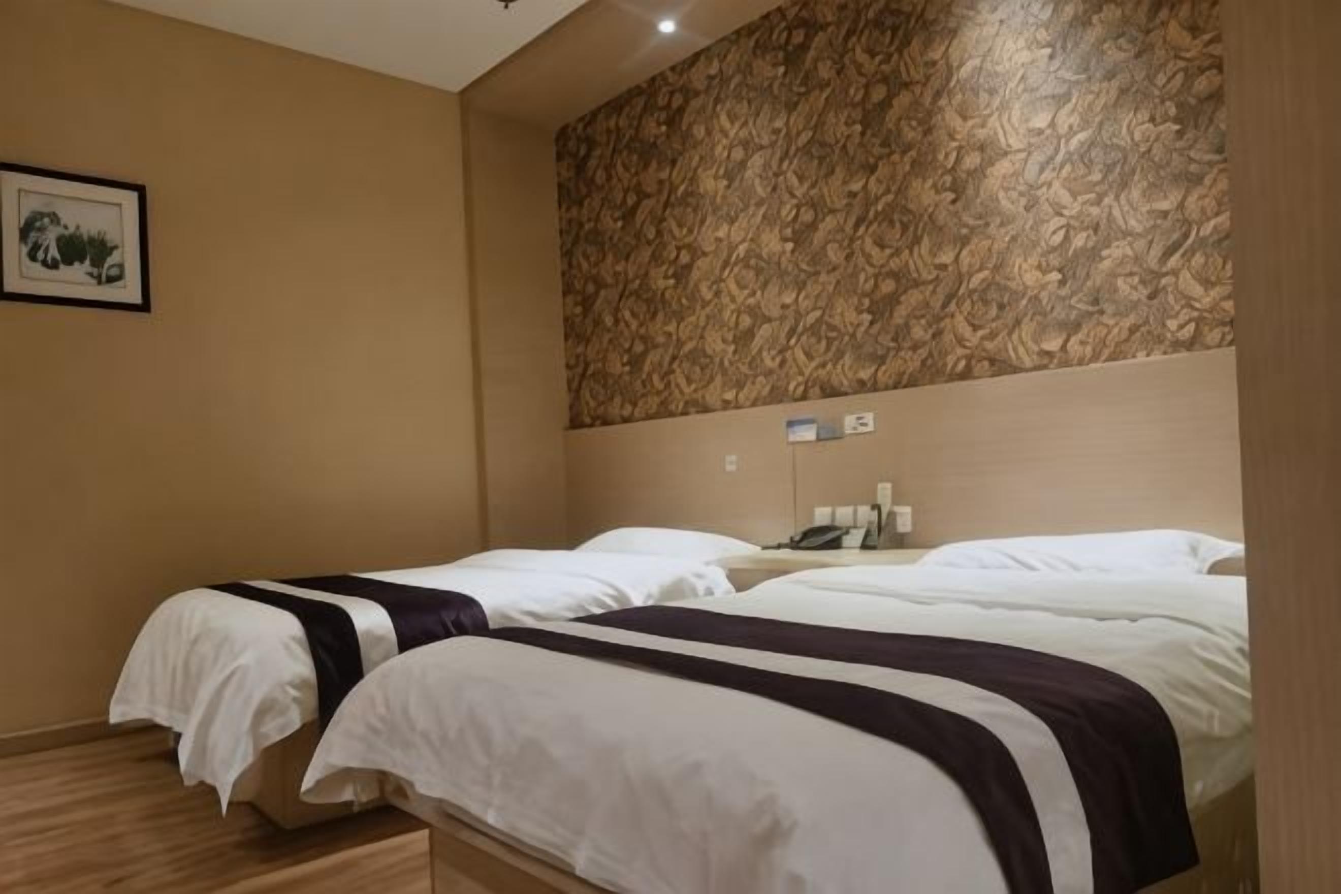 A hotel room with two beds, a patterned wall, a framed picture, and a bedside table with a phone.