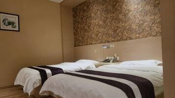 A hotel room with two beds, a patterned wall, a framed picture, and a bedside table with a phone.