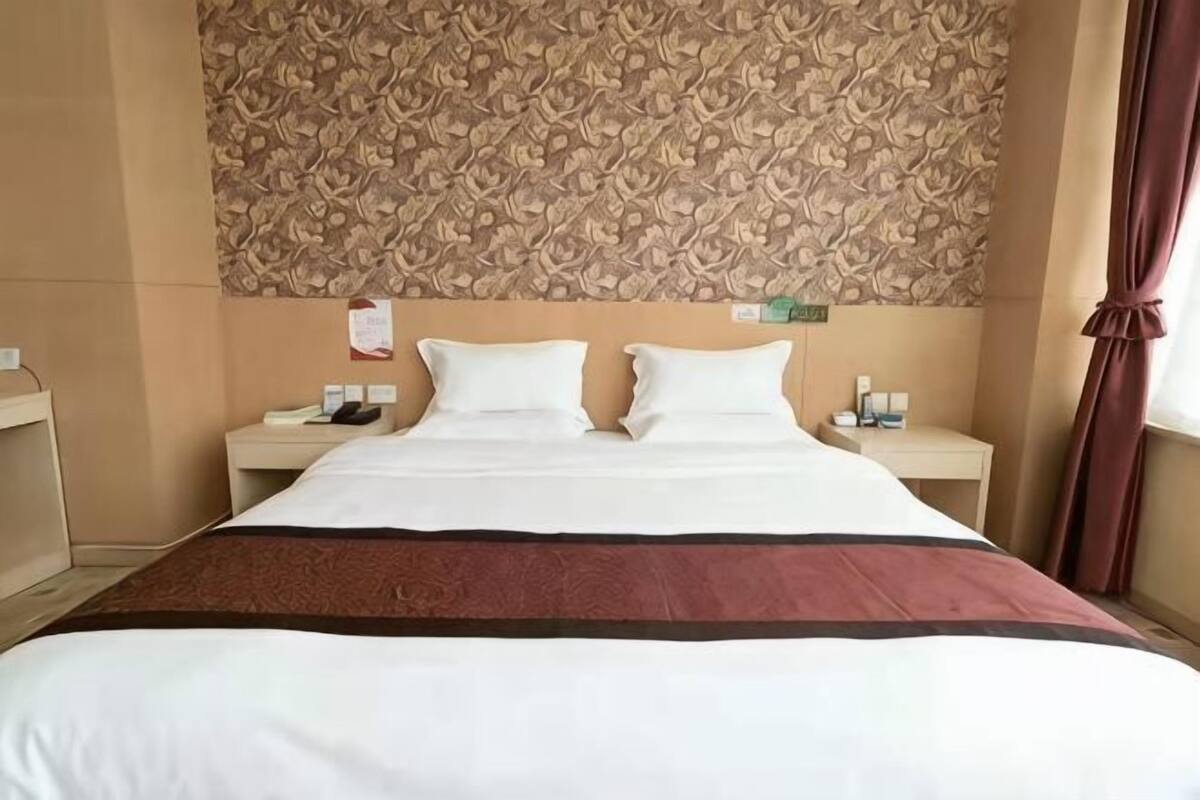 Une chambre d’hôtel avec un grand lit, deux tables de chevet, une tête de lit à motifs et une fenêtre avec des rideaux.